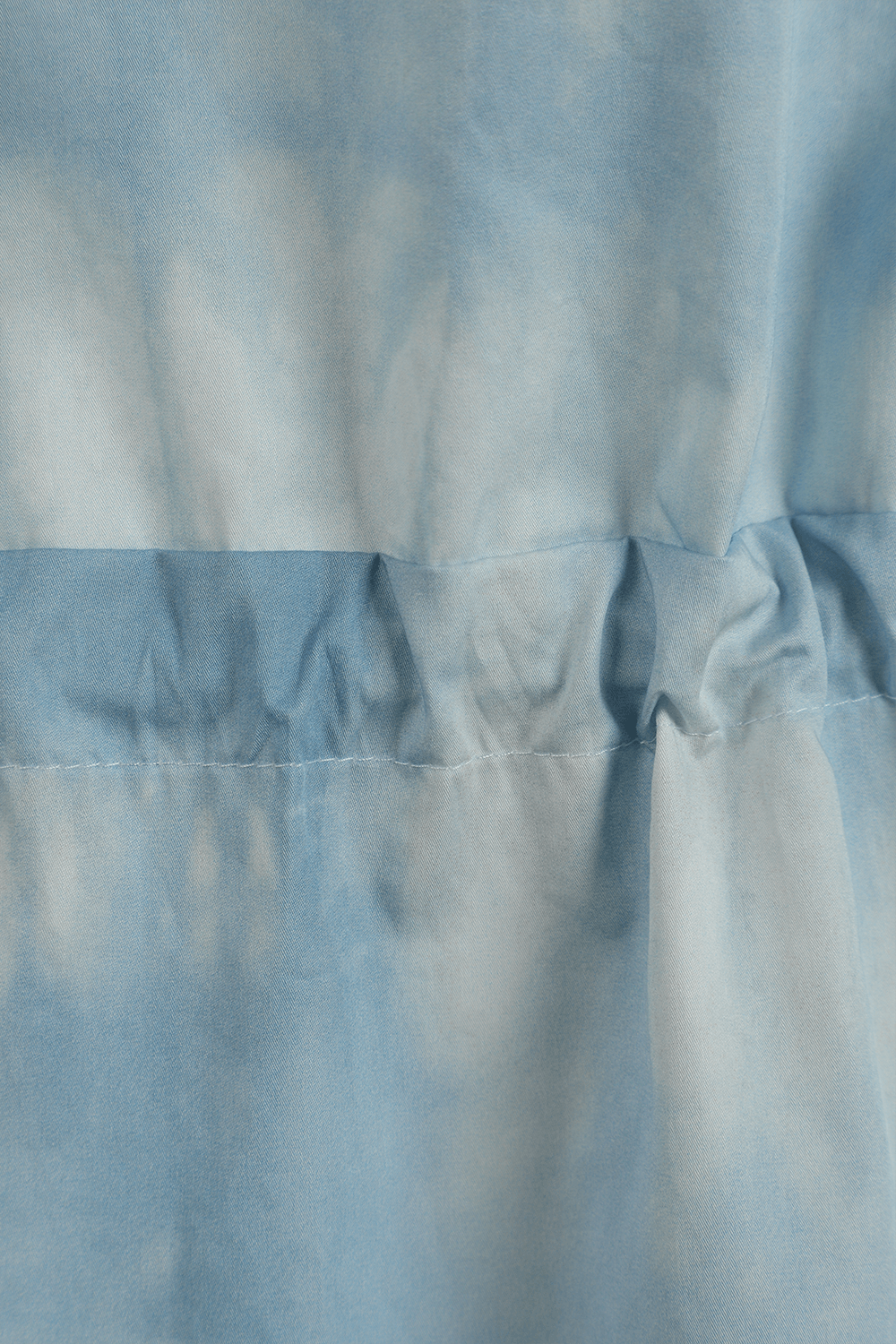 תמונת תקריב של חולצה לבנה עם קשירה ופרינט טאי-דאי תכלת